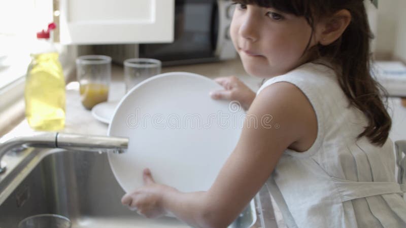 Menina séria lavando prato sozinha