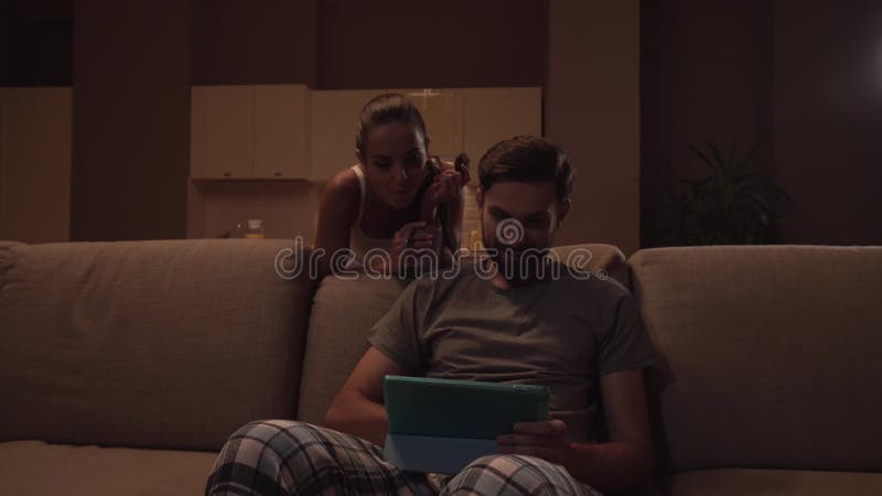 A menina toma uma cookie e anda longe da cozinha Guarda o copo Stoppes da mulher atrás do sofá onde o indivíduo se senta e se gua