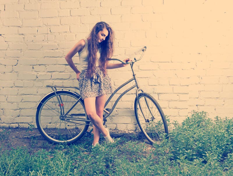 A menina triste com sua bicicleta urbana que está perto da parede branca e que olha para baixo nos pés, instagram de vista retro foto de stock A menina triste com sua bicicleta urbana que está perto da parede branca e que olha para baixo nos pés, instagram de vista retro foto de stock
