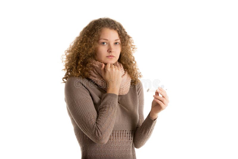 Sad girl dressed in warm dress and scarf holds thermometer looking in camera. Sad girl dressed in warm dress and scarf holds thermometer looking in camera