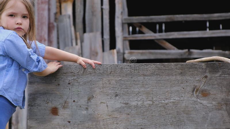 Menina triste na roupa azul empilhada em uma barreira de madeira