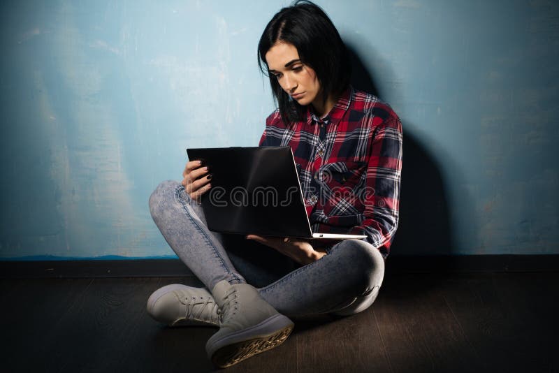 Menina triste nova que sofre da dependência nas redes sociais que sentam-se no assoalho com um caderno imagem de stock royalty free Menina triste nova que sofre da dependência nas redes sociais que sentam-se no assoalho com um caderno imagem de stock royalty free