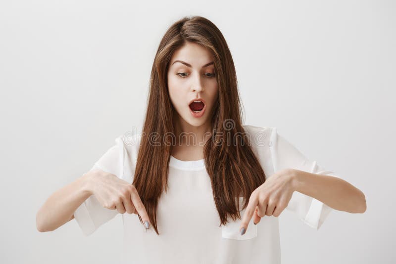 A menina é posição surpreendida no assoalho transparente Retrato da mulher atrativa oprimida que aponta para baixo com indicadore foto de stock royalty free A menina é posição surpreendida no assoalho transparente Retrato da mulher atrativa oprimida que aponta para baixo com indicadore foto de stock royalty free