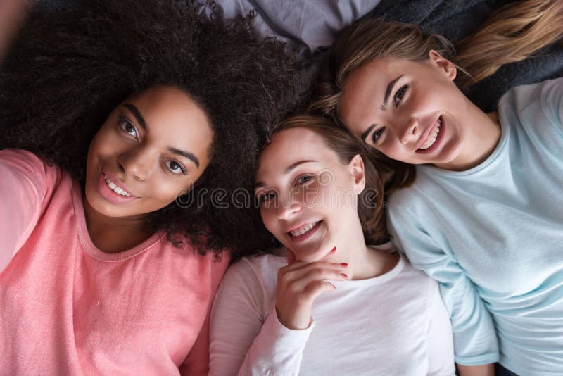 Meninas deleitadas que tomam o selfie que encontra-se na cama fotografia de stock royalty free Meninas deleitadas que tomam o selfie que encontra-se na cama fotografia de stock royalty free