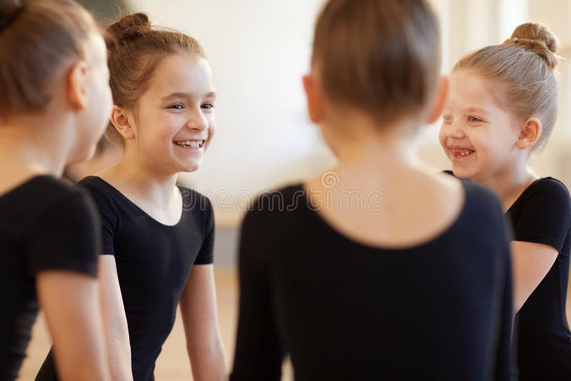 Group of cute girls giggling while sitting in circle during ballet class in studio lit by warm sunlight. Group of cute girls giggling while sitting in circle during ballet class in studio lit by warm sunlight