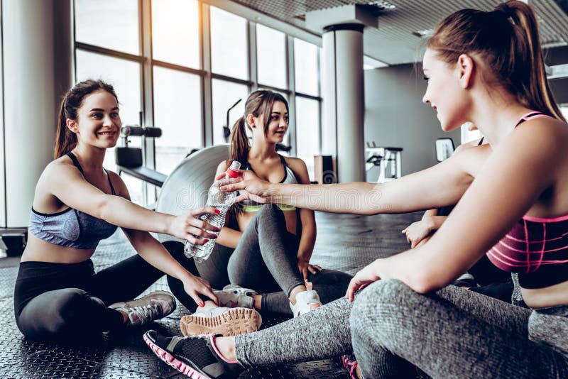 Meninas que relaxam após o exercício e a água potável imagem de stock royalty free Meninas que relaxam após o exercício e a água potável imagem de stock royalty free