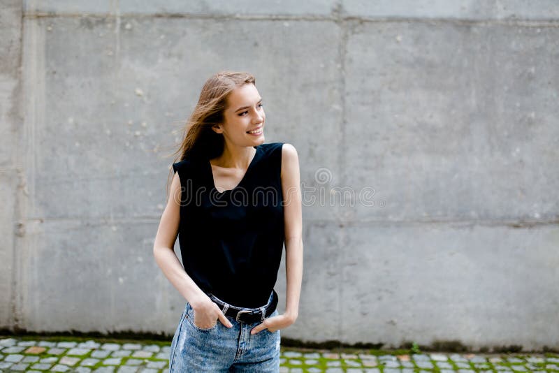 Mening van vrij jong wijfje die zich in de straat tegen grijze muur bevinden stock afbeelding Mening van vrij jong wijfje die zich in de straat tegen grijze muur bevinden stock afbeelding
