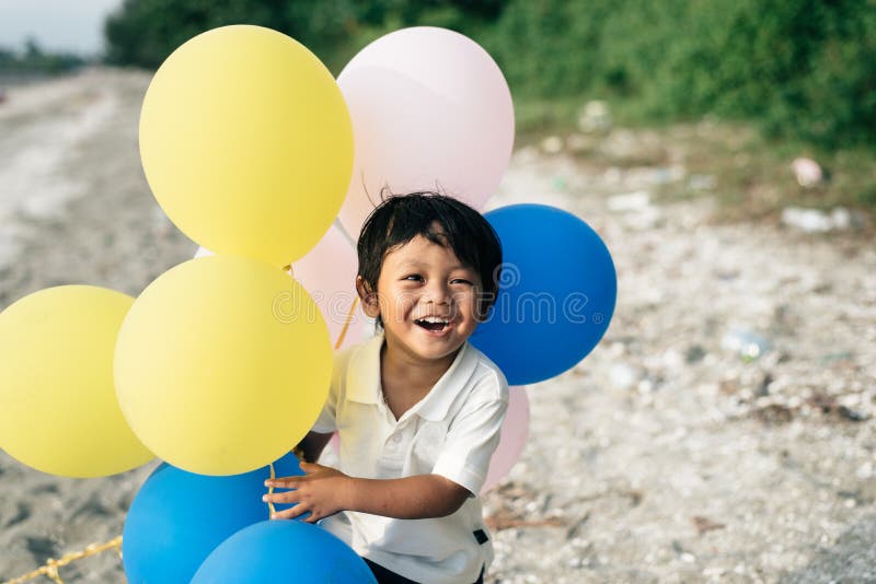 Menino asiático novo que sorri e que ri ao guardar balões imagem de stock Menino asiático novo que sorri e que ri ao guardar balões imagem de stock