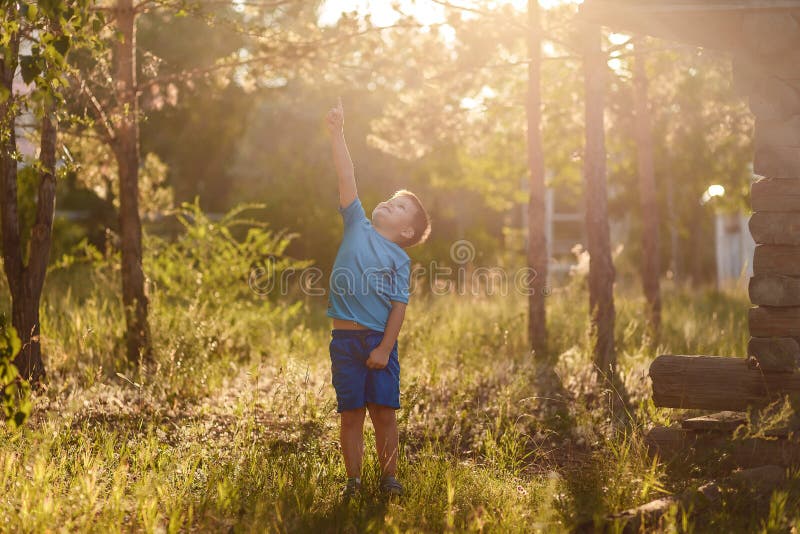 Menino caucasiano de cinco anos em um t-shirt azul e suportes do short na luz solar no verão na natureza imagens de stock Menino caucasiano de cinco anos em um t-shirt azul e suportes do short na luz solar no verão na natureza imagens de stock