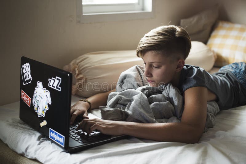 Menino caucasiano novo que encontra-se usando o portátil do computador na cama fotos de stock Menino caucasiano novo que encontra-se usando o portátil do computador na cama fotos de stock