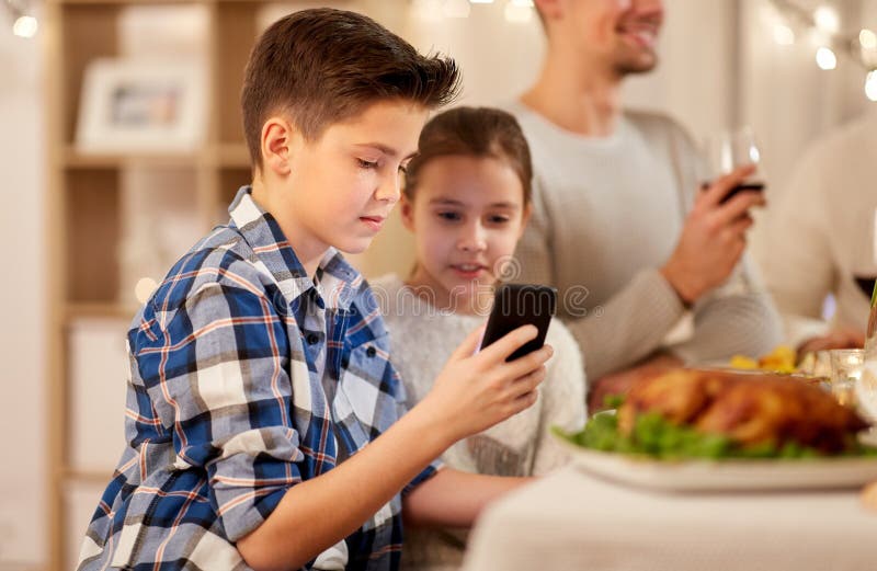 Menino com a irm? que usa o smartphone no jantar da fam?lia imagem de stock Menino com a irm? que usa o smartphone no jantar da fam?lia imagem de stock