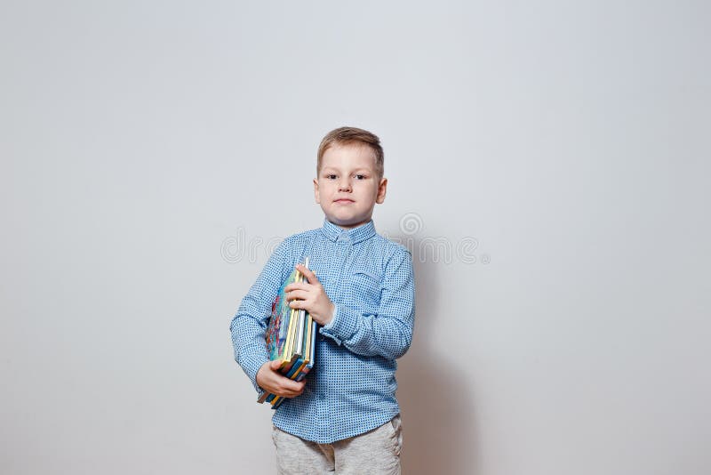 Menino considerável em uma camisa azul que guarda o livro sob seu braço foto de stock royalty free Menino considerável em uma camisa azul que guarda o livro sob seu braço foto de stock royalty free