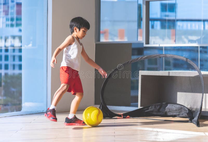 Menino Do Jogador De Futebol Que Pisa Na Bola Na Sala Imagem de