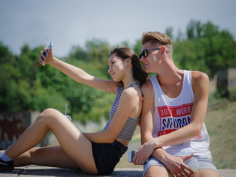 Menino e menina de sorriso felizes em um fundo do parque Noivo e amiga que tomam imagens Conceito progressivo da juventude imagem de stock Menino e menina de sorriso felizes em um fundo do parque Noivo e amiga que tomam imagens Conceito progressivo da juventude imagem de stock