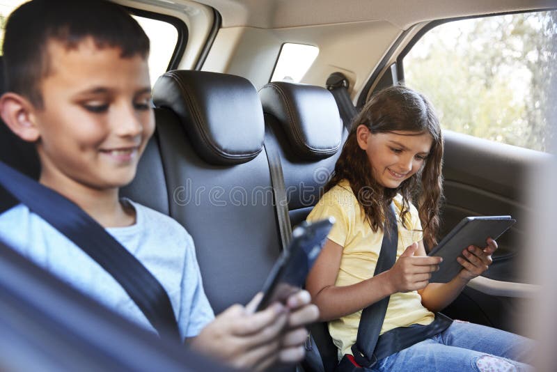 Menino e menina em um carro usando tabuletas durante a viagem por estrada da família