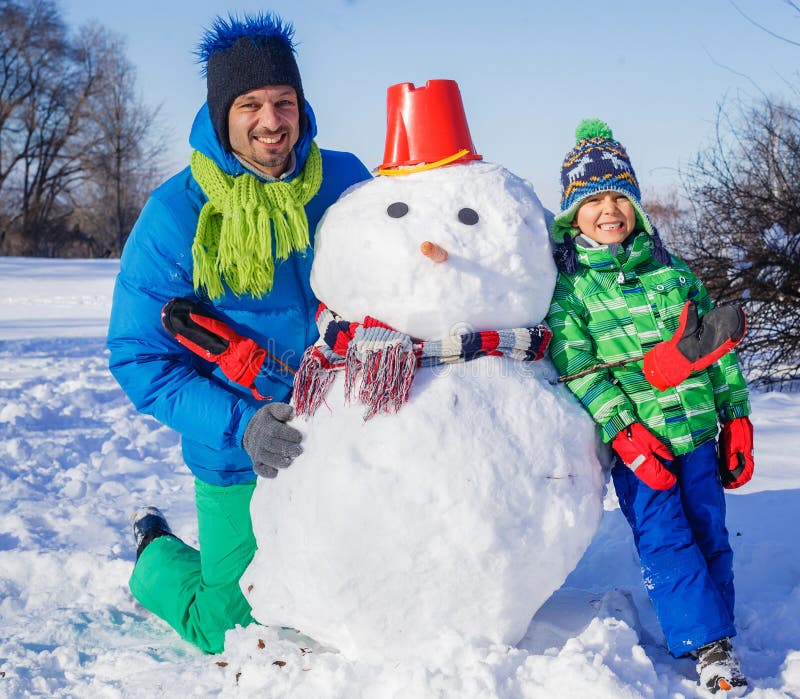 Menino e seu pai com um boneco de neve. Rapaz pequeno com seu pai que faz um boneco de neve