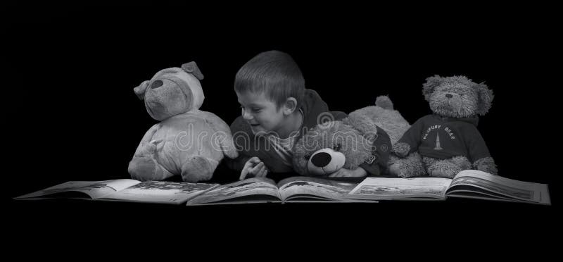 Menino engraçado com os bichos de pelúcia que leem um livro antes do tempo AR da cama foto de stock royalty free Menino engraçado com os bichos de pelúcia que leem um livro antes do tempo AR da cama foto de stock royalty free