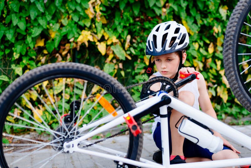 Menino feliz em um capacete da bicicleta que repara sua bicicleta imagens de stock royalty free Menino feliz em um capacete da bicicleta que repara sua bicicleta imagens de stock royalty free