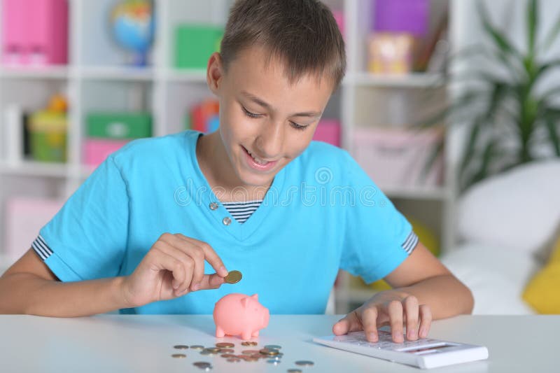 Menino jogando moedas no porquinho do banco enquanto sentado à mesa imagens de stock royalty free