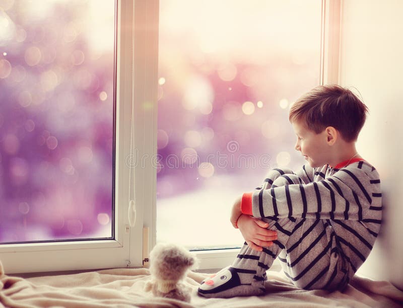 Cute little boy sitting on the windowsill in the winter window. Cute little boy sitting on the windowsill in the winter window