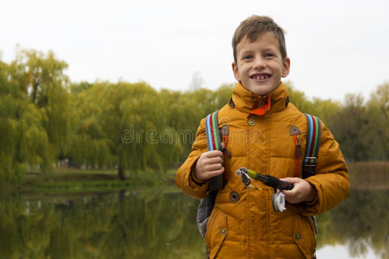 Menino no revestimento amarelo que guarda a vara de pesca fora na lagoa durante o dia fresco do outono imagens de stock royalty free Menino no revestimento amarelo que guarda a vara de pesca fora na lagoa durante o dia fresco do outono imagens de stock royalty free
