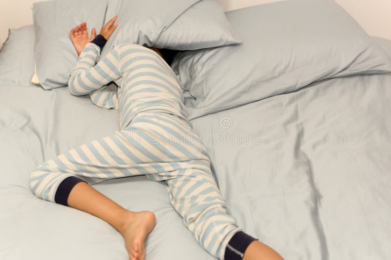 Menino novo que dorme na cama com sua cabeça sob o descanso em casa fotos de stock Menino novo que dorme na cama com sua cabeça sob o descanso em casa fotos de stock