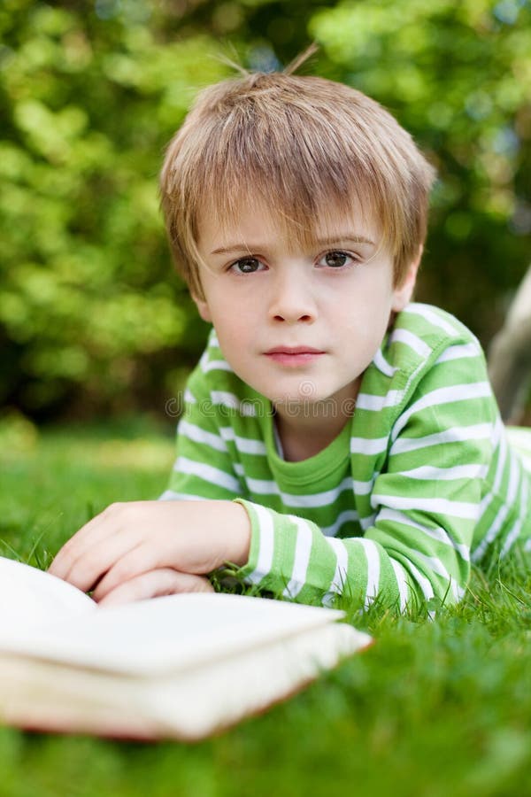 Menino novo que olha acima de ler um livro imagens de stock Menino novo que olha acima de ler um livro imagens de stock