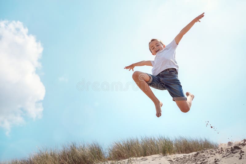 Menino que corre e que salta sobre a duna de areia em férias da praia foto de stock Menino que corre e que salta sobre a duna de areia em férias da praia foto de stock