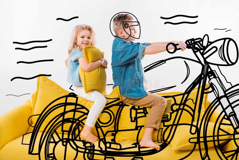 menino que finge ser um motociclista e um velomotor de montada ao sentar-se no sofá amarelo imagem de stock menino que finge ser um motociclista e um velomotor de montada ao sentar-se no sofá amarelo imagem de stock