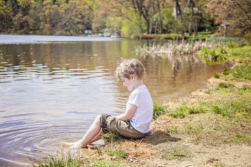 Menino que senta-se na costa do lago imagens de stock Menino que senta-se na costa do lago imagens de stock