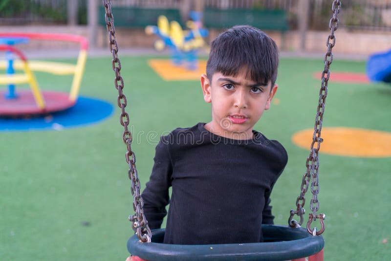 Menino triste irritado que senta-se no balanço foto de stock Menino triste irritado que senta-se no balanço foto de stock