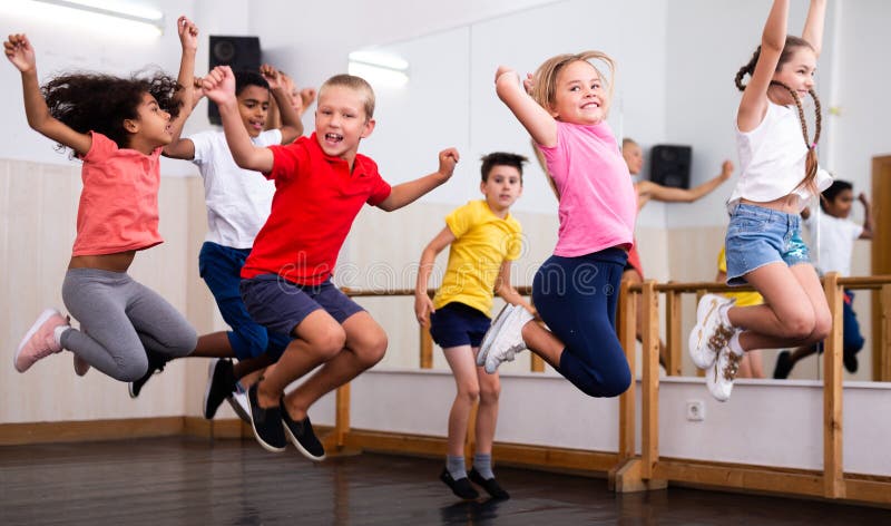 Cheerful preteen boys and girls having fun in group dance class, jumping with female coach . Cheerful preteen boys and girls having fun in group dance class, jumping with female coach ..