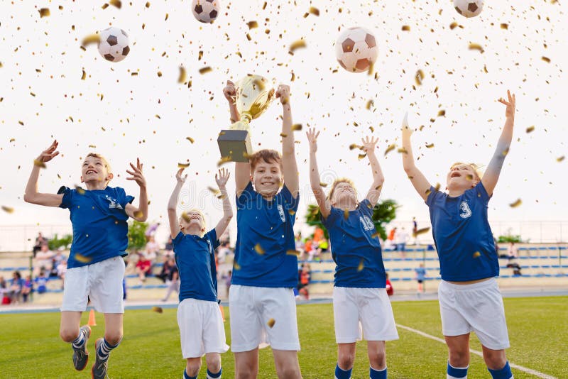 Meninos felizes que comemoram o campeonato do futebol Futebol da juventude que ganha Team Jumping e o copo dourado de aumentação