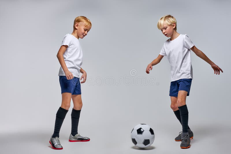 Dois Jogadores De Futebol Chutando Bola De Futebol Em Um Jogo. Meninos Da  Escola Jogam Competição Esportiva. Duas Crianças Multirraciais Jogando  Partida De Futebol. Crianças Em Uniformes De Futebol Verde E Azul