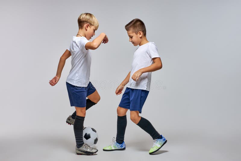 Dois Jogadores De Futebol Chutando Bola De Futebol Em Um Jogo. Meninos Da  Escola Jogam Competição Esportiva. Duas Crianças Multirraciais Jogando  Partida De Futebol. Crianças Em Uniformes De Futebol Verde E Azul