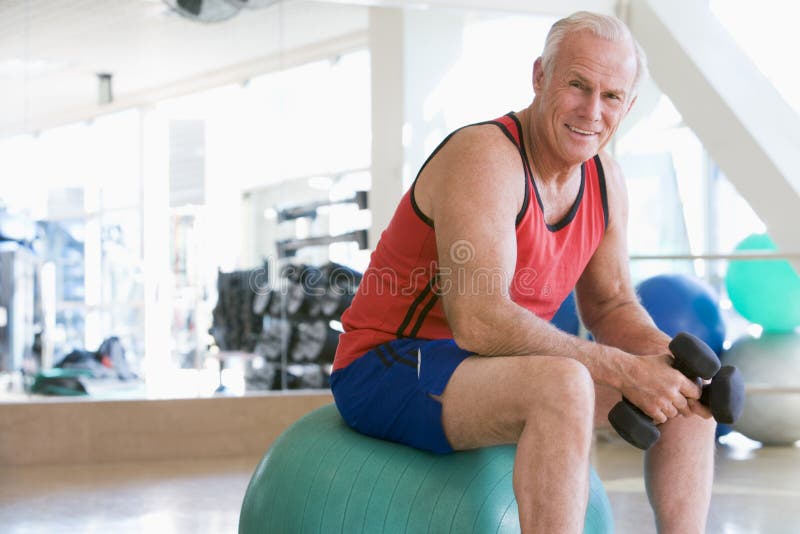 Mens die de Gewichten van de Hand op Zwitserse Bal gebruikt bij Gymnastiek royalty-vrije stock foto Mens die de Gewichten van de Hand op Zwitserse Bal gebruikt bij Gymnastiek royalty-vrije stock foto