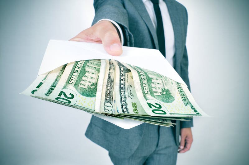 A man in suit giving an envelope full of american dollar bills. A man in suit giving an envelope full of american dollar bills