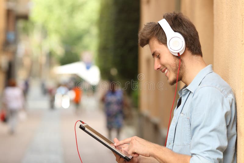 Mens die een tablet met hoofdtelefoons op de straat gebruiken stock fotografie Mens die een tablet met hoofdtelefoons op de straat gebruiken stock fotografie