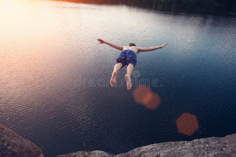 Young man jumping into the water from cliff at sunset with outspread hands. Young man jumping into the water from cliff at sunset with outspread hands