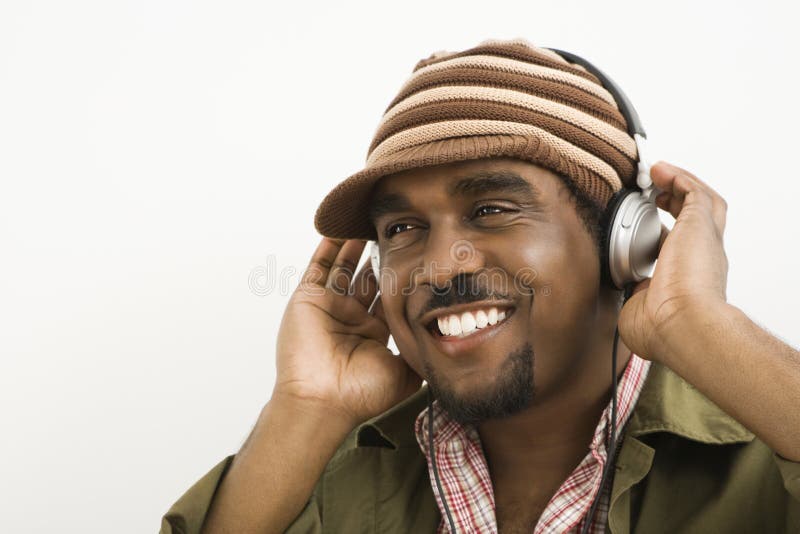 African-American mid-adult man wearing knit hat and listening to headphones smiling. African-American mid-adult man wearing knit hat and listening to headphones smiling.