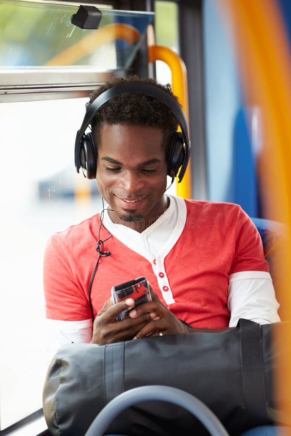Man Wearing Headphones Listening To Music On Bus Journey Holding Mobile Phone Device. Man Wearing Headphones Listening To Music On Bus Journey Holding Mobile Phone Device