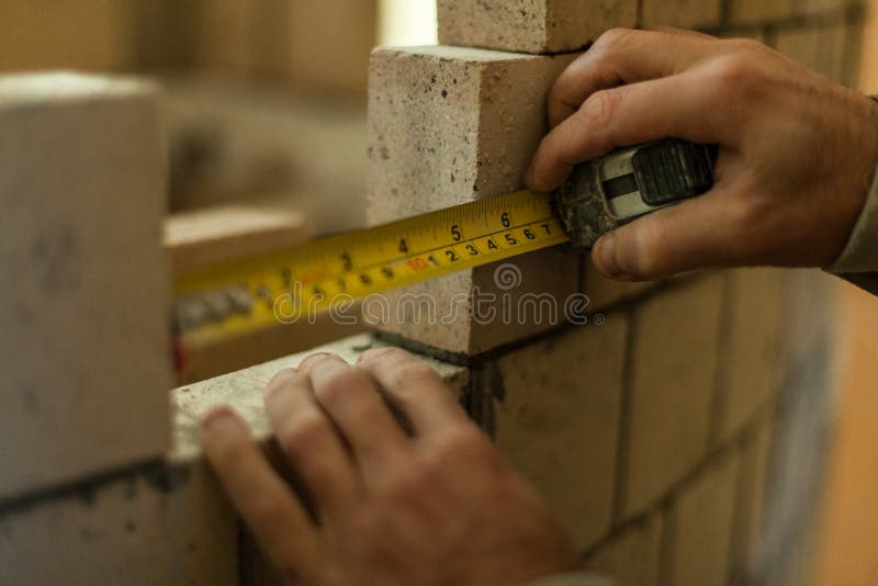 Mens die metingen maken terwijl het werken aan zijn bakstenen muur royalty-vrije stock foto Mens die metingen maken terwijl het werken aan zijn bakstenen muur royalty-vrije stock foto