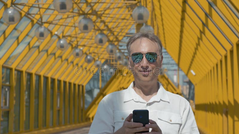 Mens die op middelbare leeftijd in grote spiegelglazen foto's op een smartphone bekijken