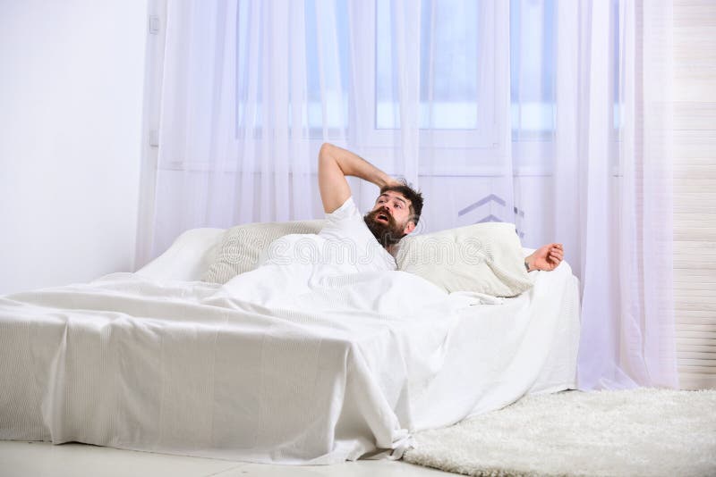 Mens die in overhemd op bed wakker, wit gordijn leggen op achtergrond Kerel op geschokte gezichtsontwaken in ochtend Macho met stock afbeelding Mens die in overhemd op bed wakker, wit gordijn leggen op achtergrond Kerel op geschokte gezichtsontwaken in ochtend Macho met stock afbeelding