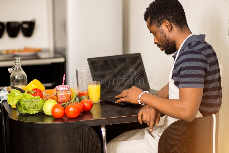 Mens die thuis recept op laptop in keuken kijken stock afbeelding Mens die thuis recept op laptop in keuken kijken stock afbeelding