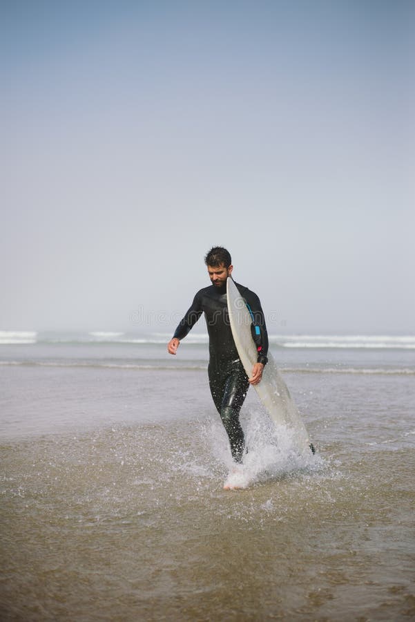 Mens die in wetsuit het water na het surfen verlaten stock afbeelding Mens die in wetsuit het water na het surfen verlaten stock afbeelding