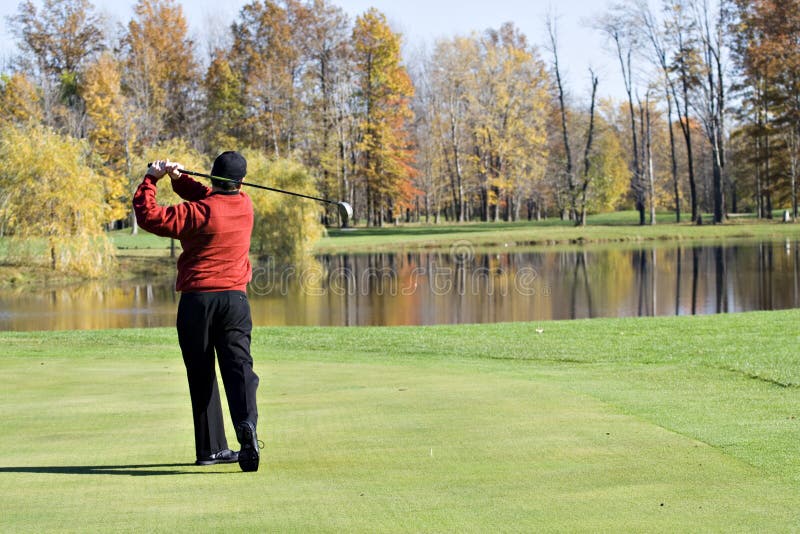 A male golfer smartly dressed in a red sweater is enjoying a round of November golf. A male golfer smartly dressed in a red sweater is enjoying a round of November golf.