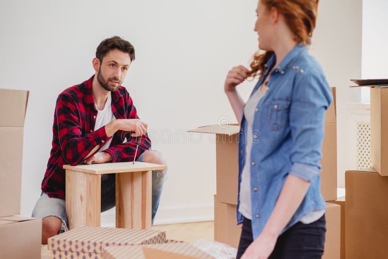 Mens het assembleren meubilair terwijl het leveren van nieuw huis na verhuizing met vrouw royalty-vrije stock foto's Mens het assembleren meubilair terwijl het leveren van nieuw huis na verhuizing met vrouw royalty-vrije stock foto's
