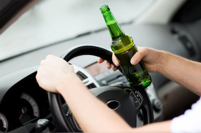 Transportation and vehicle concept - man drinking alcohol while driving the car. Transportation and vehicle concept - man drinking alcohol while driving the car