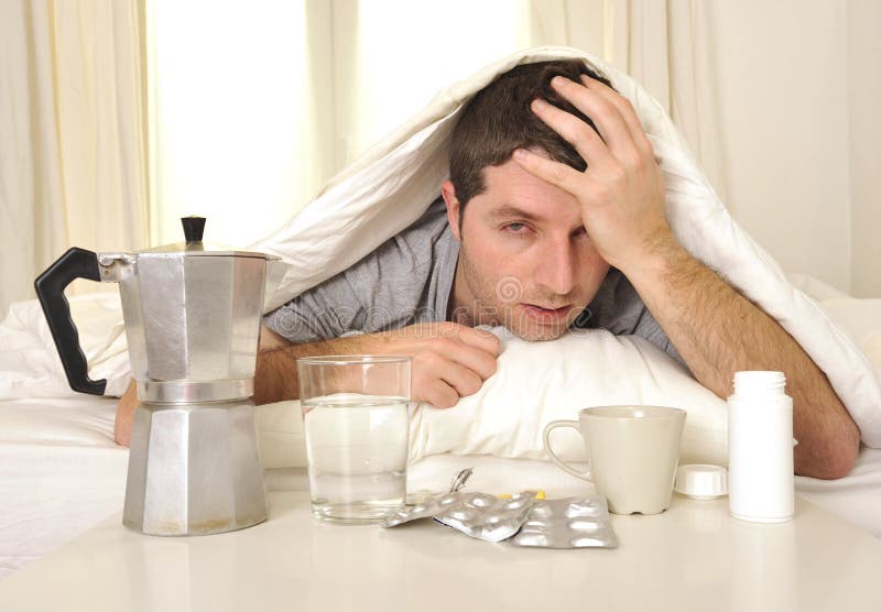 Mens met hoofdpijn en kater in bed met tabletten royalty-vrije stock afbeelding Mens met hoofdpijn en kater in bed met tabletten royalty-vrije stock afbeelding